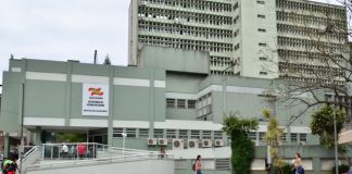 fachada do prédio do hospital vista do outro lado da rua; mulher passa na calçada