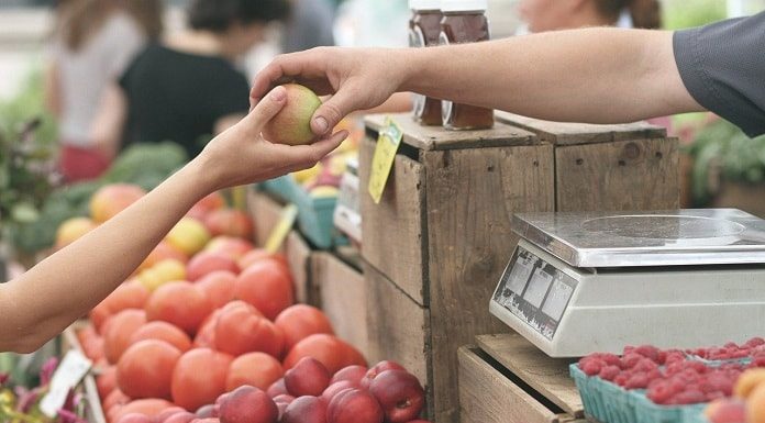 comerciante entrega maça à mão de mulher sobre prateleira de frutas