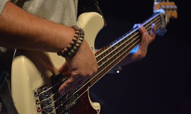 close em homem tocando contrabaixo; ele usa duas pulseiras na mão direita