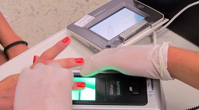 pessoa usando luvas tomas as digitais de mulher em aparelho de biometria