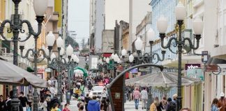 algumas mulheres de máscara andando no calçadão da felipe schimidt no centro de florianópolis; viatura ao fundo