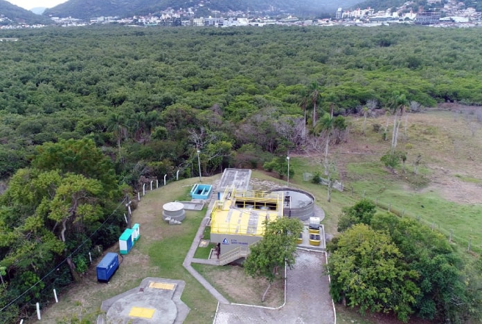 foto aérea de estação de tratamento de esgoto ao lado de grande área de mata