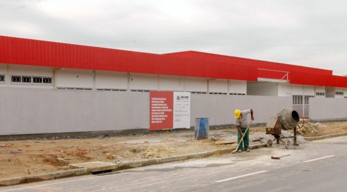 parte externa de creche com operário retirando areia do meio fio e betoneira ao lado