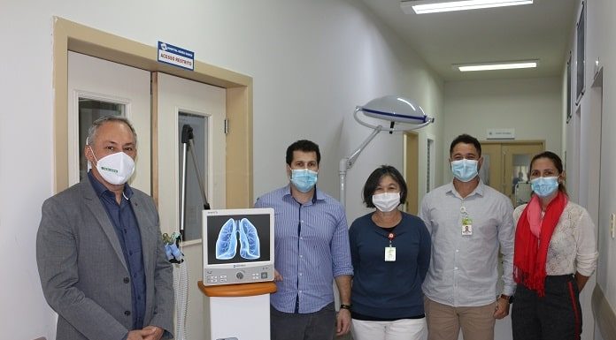 cinco pessoas usando máscara posam para a foto no corredor do hospital ao lado do respirador