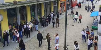 imagem de câmera de segurança sobre rua felipe schmidt no centro de florianópolis mostra pessoas espalhadas e andando pelo caldação, algumas paradas em frente aos comércios. todas de máscaras. poste no meio