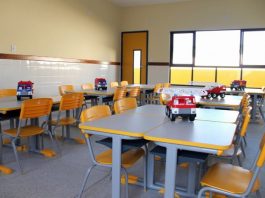 sala de aula com carteiras e cadeiras organizadas com caminhão de brinque sobre a mesa