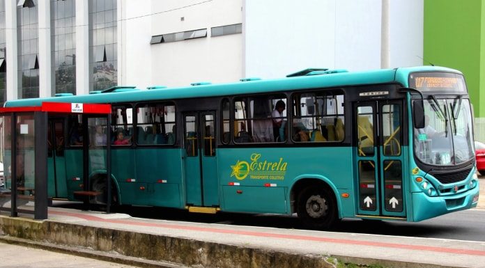 ônibus verde da empresa estrela visto de lado parado em frente a ponto de ônibus com algumas pessoas