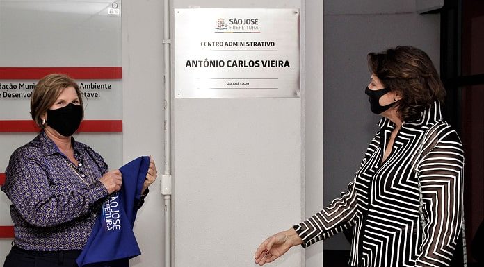 adeliana e margaret ao lado da placa com o nome de antonio carlos vieira; ambas usam máscara