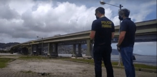 dois policiais federais de costas olham para drone no céu ao lado das pontes de florianópolis