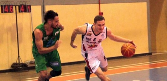 jogador de verde acompanha jogador de branco com a bola de basquete na quadra