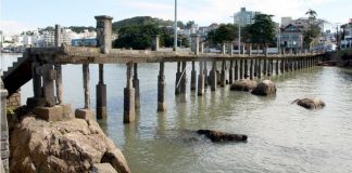 trapiche visto de lado com as palafitas comprometidas; pedras na água; bairro ao fundo