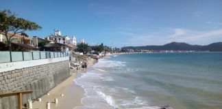 praia dos ingleses, com mar batendo nos muros da orla; guarda corpo de madeira em primeiro plano; praia ao longo até o fundo da foto