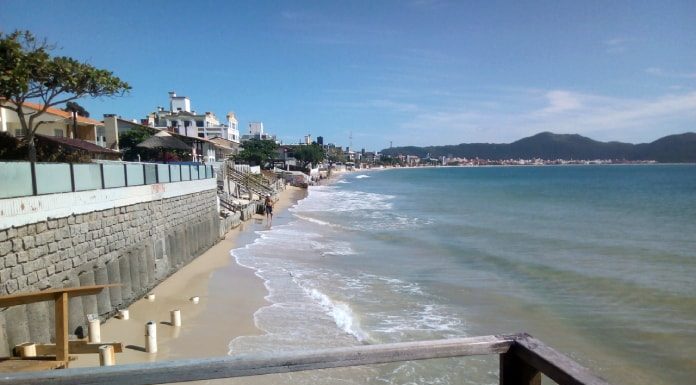 praia dos ingleses, com mar batendo nos muros da orla; guarda corpo de madeira em primeiro plano; praia ao longo até o fundo da foto