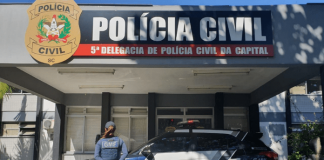 Fachada da Delegacia da Polícia Civil, com um carro da Guarda Municipal e uma policial com colete da GMF à frente