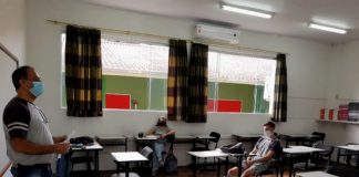 professor usando máscara dá aula para dois alunos, maioria das carteiras vazias