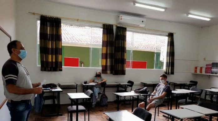 professor usando máscara dá aula para dois alunos, maioria das carteiras vazias