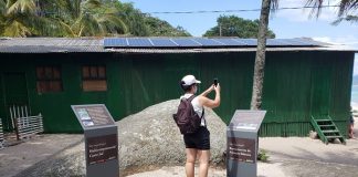 Mulher tira fotos no sítio arqueológico da ilha do Campeche, ela está próxima às placas instaladas com informações do local.