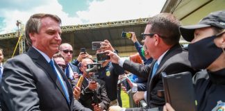 bolsonaro sorridente aperta mão de agente da prf com pesosas em volta filmando com celulares; algumas sem máscara; presidente sem máscara