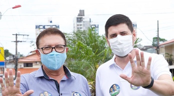 orvino e michel schlemper fazem o número cinco com as mãos para a foto; ambos usam máscara