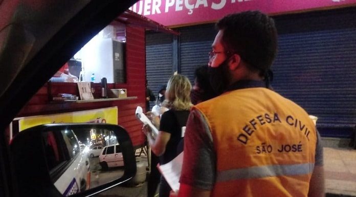 em são josé órgão de fiscalização orientam comércios sobre decreto da madrugada - fiscal da defesa civil visto de costas com logo no colete, em frente a barraquinha de cachorro quente