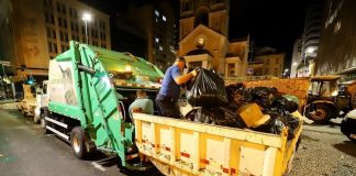 caminhão com caçamba carregada de lixo ao lado de caminhão de lixo estacionado no largo da matriz