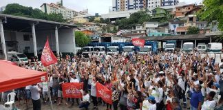 termina a greve da comcap com acordo de reajuste; centenas de pessoas reunidas em pátio da companhia; muitas com os braços para cima; tenda do sindicato à frente; caminhões ao fundo