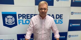 gean posa para a foto com os chips de celulares para os estudantes de florianópolis; painel da prefeitura ao fundo