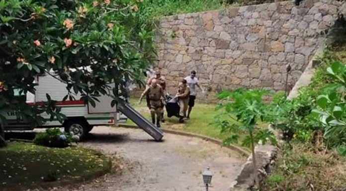 Polícia mata: policias carregando saco com corpo de um dos ladrões mortos na ponta de baixo para uma viatura do iml