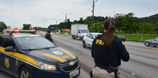 Policial de costas ao lado do carro da PRF na rodovia