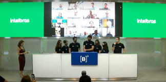 Seis representantes da Intelbras em evento que marca estreia da empresa na bolsa de valores. Ao fundo três telas, a do meio com participantes do evento em chamada de vídeo e as outras duas com cor verde e "Intelbras" escrito em branco.