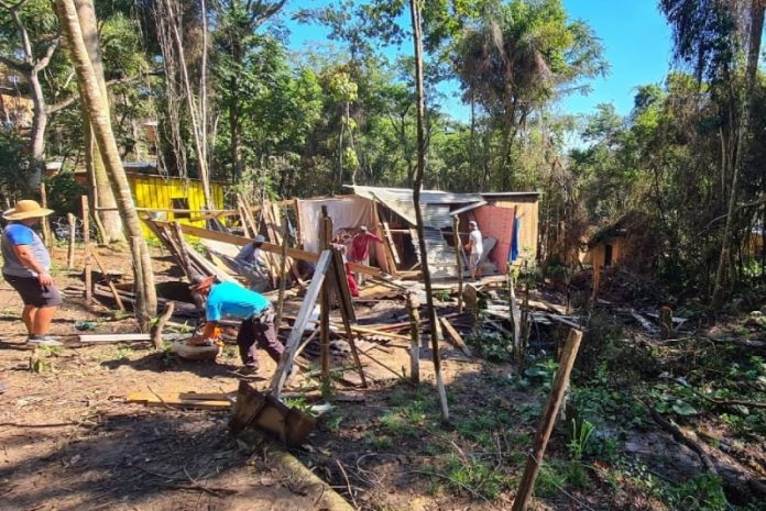 casas demolidas com operários trabalhando na retirada do material em meio à mata