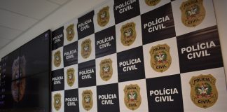 A imagem ilustra a prisão efetuado por policiais civis de um homem suspeito de estupro em São José. Painel com quadros brancos e brasão da polícia civil ao lado de quadros pretos com a escrita em branco de "polícia civil". Ao lado há um televisor.