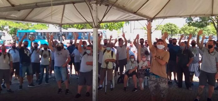 funcionários do transporte coletivo da grande florianópolis reunidos sob tenda com os braços levantados; todos usam máscaras