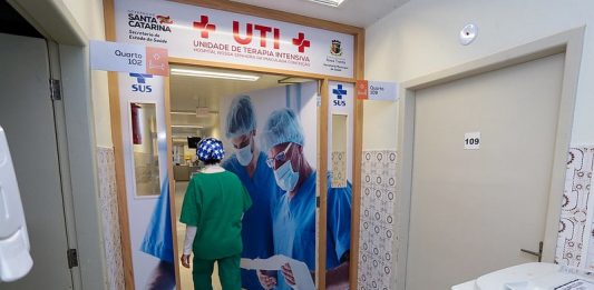 profissional de saúde com trajes entra em porta da ala de uti do hospital de nova trento