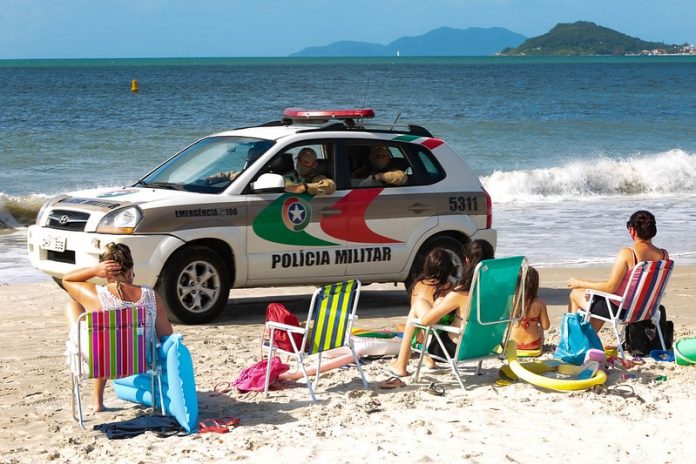 viatura suv da polícia passando por pessoas sentadas na areia da praia