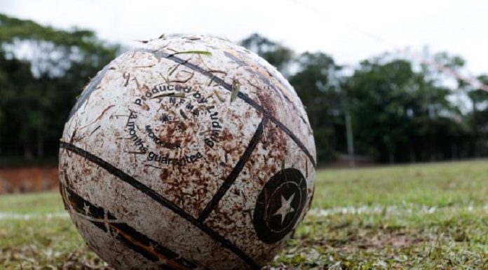 Uma bola branca suja de barro e ao fundo um campo de grama. A foto ilustra a alteração do governo no decreto de medidas restritivas, agora os esportes recreativos estão autorizados em SC.