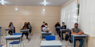 Alunos do ensino estadual de SC usam máscaras em sala de aula. É possível ver carteiras brancas com cadeiras azuis vazias.