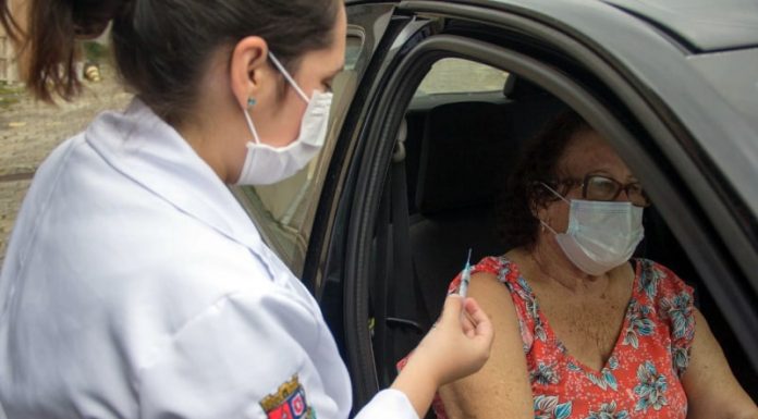 profissional de saúde com agulha na mão ao lado de senhora sentada em carro com a porta aberta