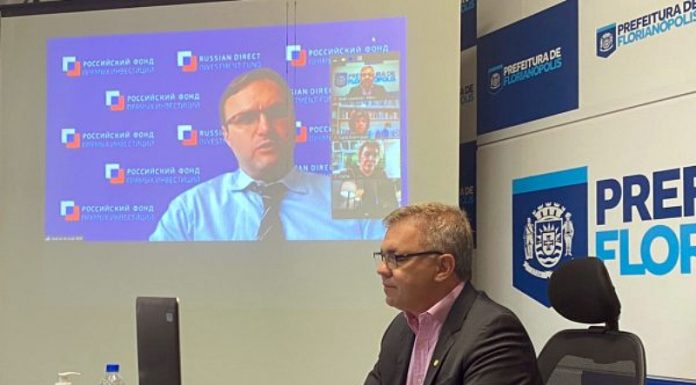 gean loureiro, presidente do consórcio conectar, em conversa online na prefeitura de florianópolis; outro homem projetado no telão ao fundo