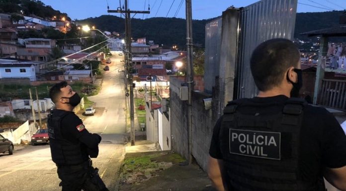 dois policiais civis olham para residência em ladeira com muitas casas ao fundo no início da 3ª fase da operação héracles