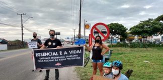 No acostamento de uma rua, grevistas seguram cartazes em que é possível ler "essencial é a vida". Três pessoas estão em pé e uma agachada com uma criança. A greve dos servidores da educação municipal de Florianópolis segue sem acordo com a prefeitura.