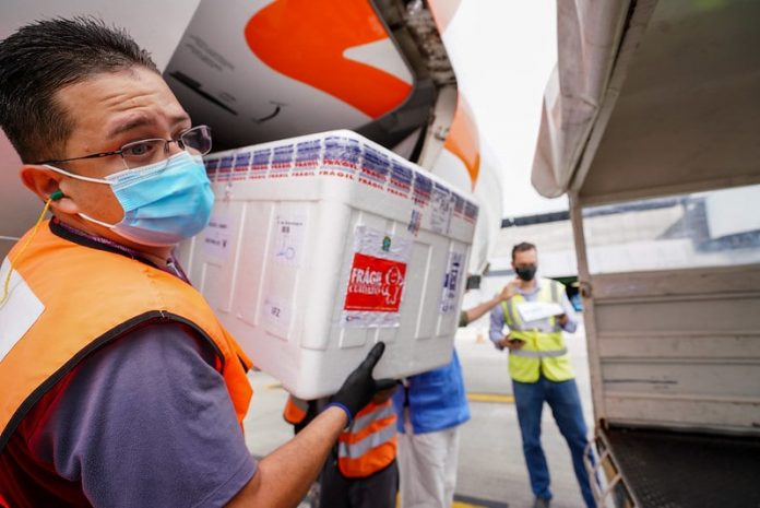 homens usando máscara retiram caixa de isopo de avião - lote de 250 mil doses chega em sc