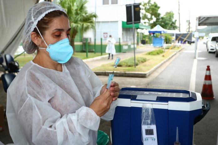 profissional de saúde usando máscara e epi maneja doses de vacina em drive-thru - vacinção de 60 anos na grande florianópolis