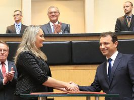 Em foto de arquivo, Daniela de roupa preta e cabelos loiros aperta a mão de Carlos Moisés, de terno escuro. Em volta é possível ver cinco homens de terno. O governador e a vice foram convocados para depor na CPI da pandemia, do senado federal.