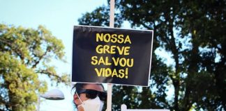 mulher usando máscara empunha placa escrita "nossa greve salvou vidas"