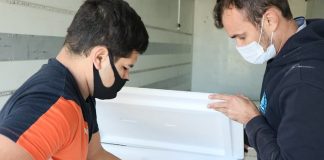 Novo lote de vacinas, com 209 mil doses, é distribuído em SC - homens conferem temperatura dentro de caixa de isopor