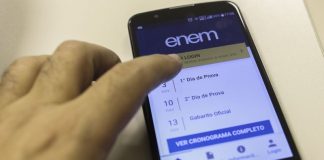 Uma mão mexe na tela de um celular em que é possível ler informações sobre o enem 2021