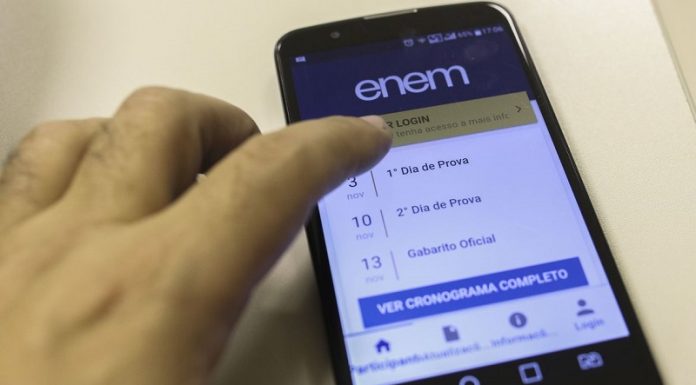 Uma mão mexe na tela de um celular em que é possível ler informações sobre o enem 2021