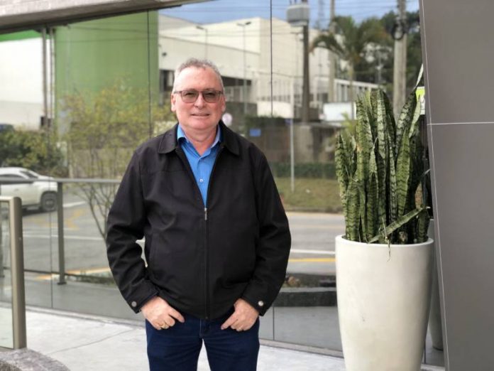 José Marciel neis posa com as mãos nos bolsos da calça, ele veste calça e jaqueta preta, além de uma camiseta azul. Ele usa óculos, tem cabelos grisalhos e pele branca. Neis será o novo presidente da Aemflo e CDL de São José.