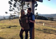 Roberta Zilli e Bruno Buske olham um para o outro em paisagem serrana segurando taça de vinho